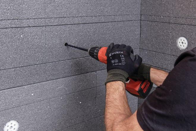 Ein Bauarbeiter bohrt ein Loch in eine VENTO Dämmplatte VENTO befestigen